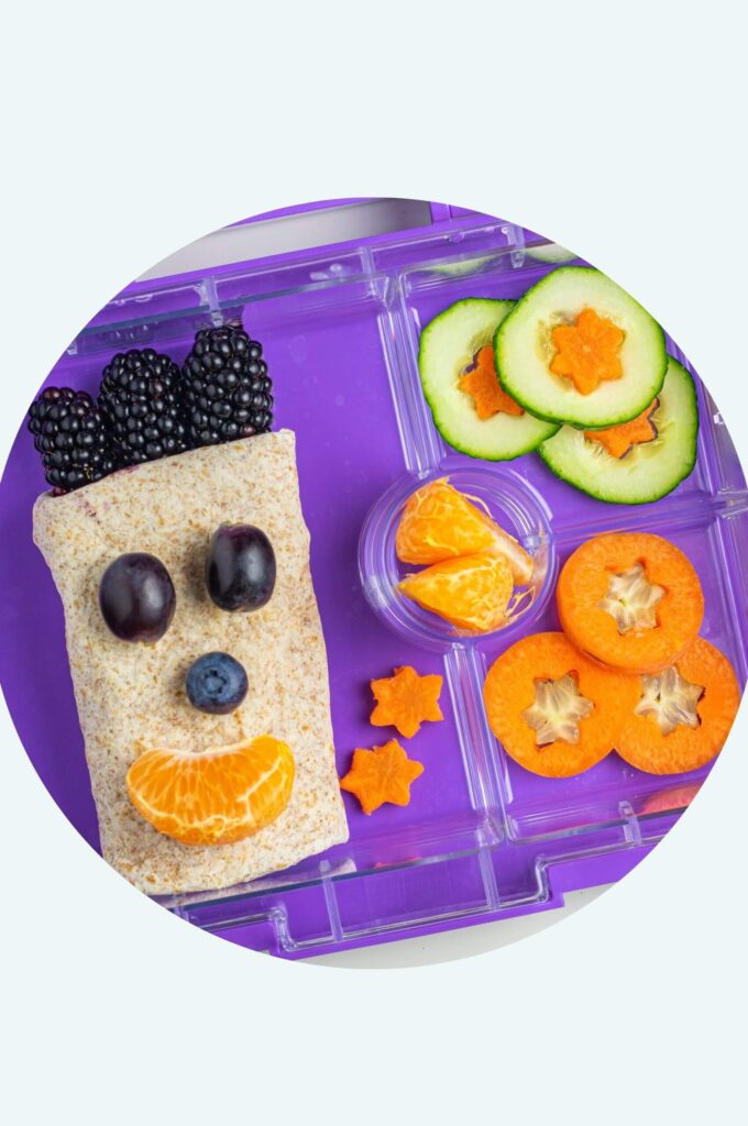 Schulpause Essen: Ein "Be Happy" Wrap mit lächelndem Gesicht aus Obst und bunten Gemüsesternen